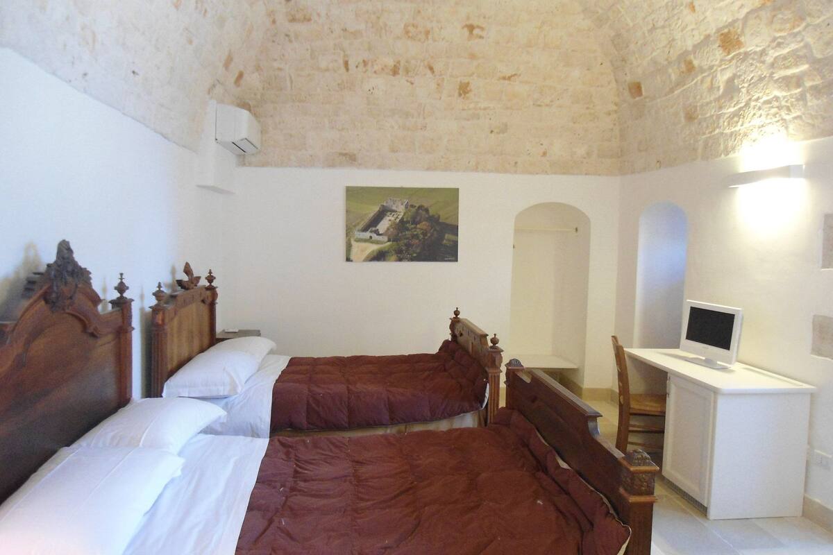 A bedroom with two wooden beds, a desk with a computer, and a painting on the wall.