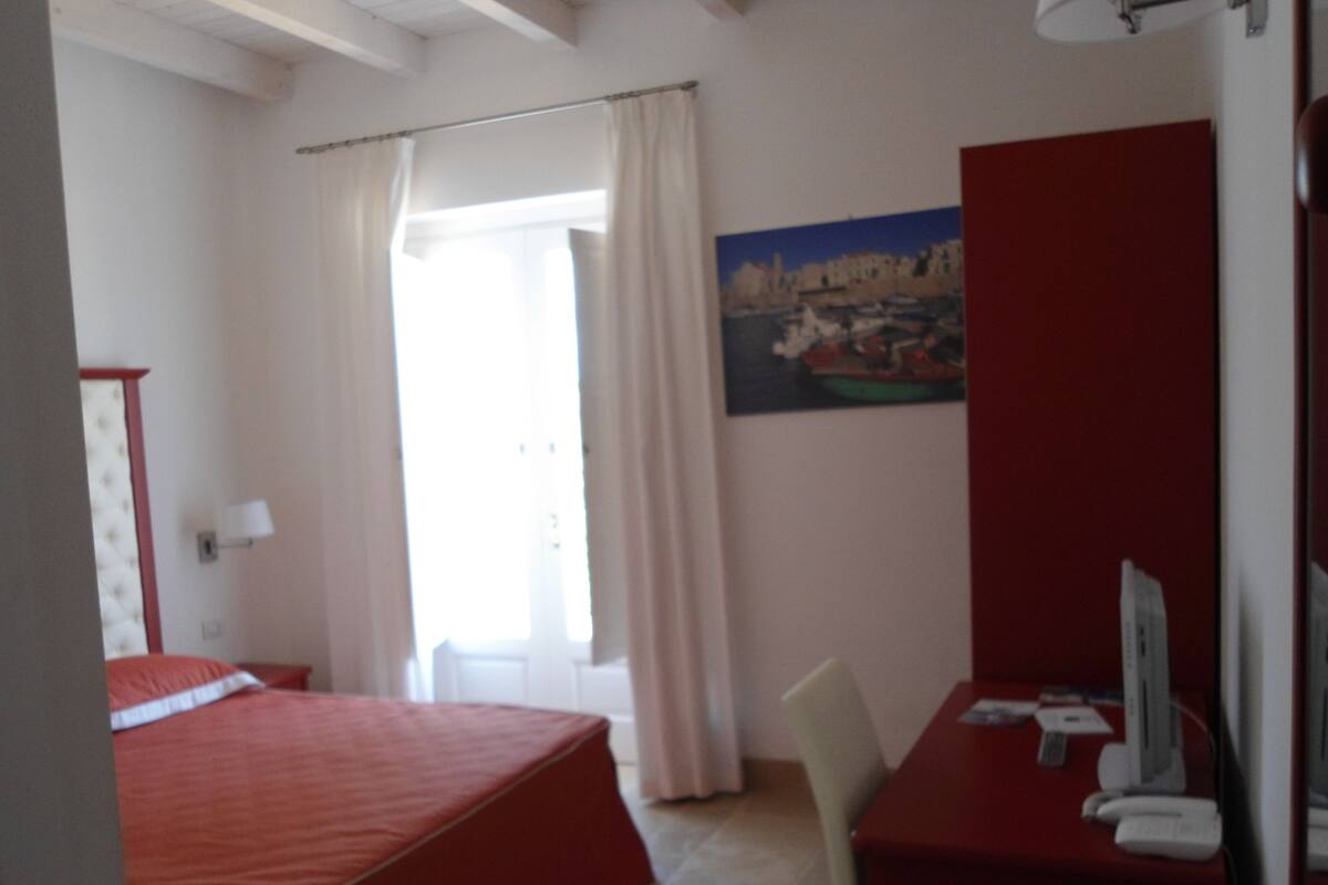 A bedroom with a bed, a desk, a chair, a computer, and a painting on the wall.