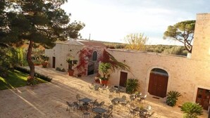 A courtyard with outdoor seating, a stone building, and surrounding greenery. - Parco dei Manieri (Conversano)