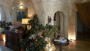 A stone-walled room with a wooden cabinet, a table with papers, and a potted plant. - Parco dei Manieri (Conversano)