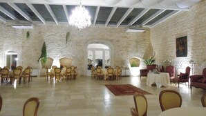A spacious room with stone walls, multiple tables and chairs, and a chandelier. - Parco dei Manieri (Conversano)