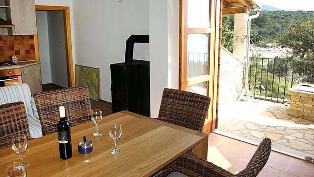 A dining area with a wooden table, wicker chairs, and a bottle of wine. - Vacation home Jure by Interhome (Pašman/Neviđane)
