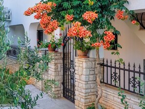 A stone wall with a metal gate, potted plants, and a flowering vine. - Apartment Danica by Interhome (Fažana/Peroj)