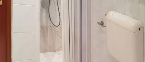 A bathroom with a shower, toilet, and a white tiled wall.