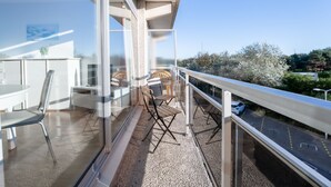 Een balkon met een tafel, stoelen, een leuning en uitzicht op een weg en groen.