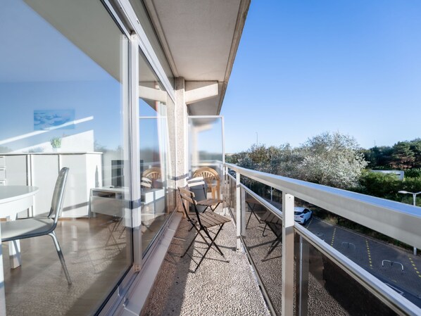 A balcony with a table and chairs, a railing, and a view of a road and greenery.