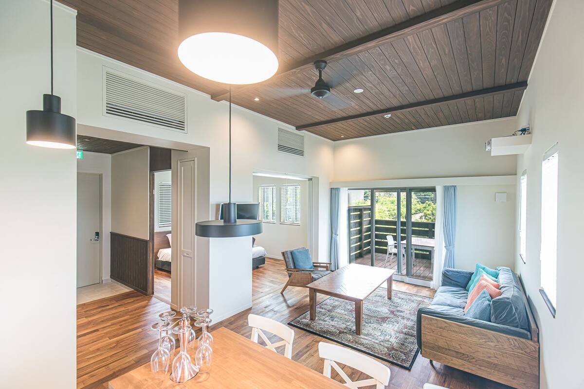 Uma sala de estar ampla com teto de madeira, uma mesa de jantar e um sofá.