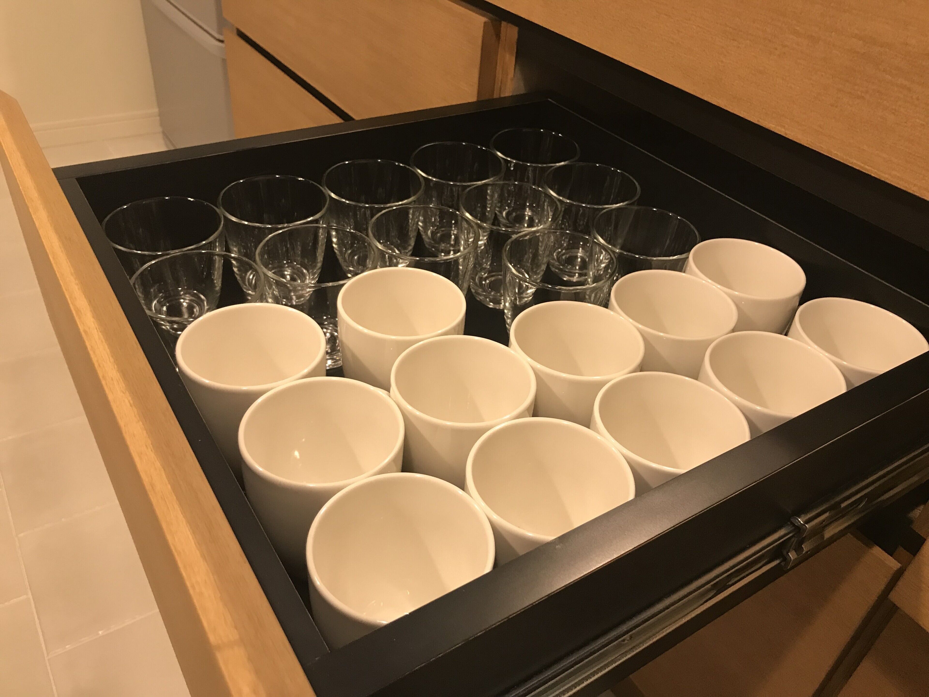 Un tiroir de cuisine contenant plusieurs tasses blanches et des verres transparents.