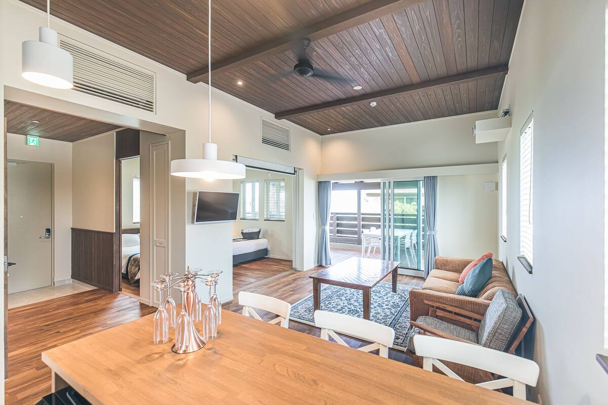Uma sala ampla com teto de madeira, uma mesa de jantar com cadeiras, um sofá e uma TV fixada na parede.