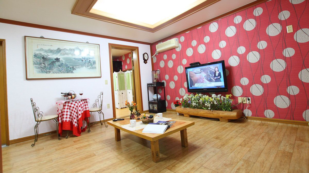 A living room with a wooden coffee table, a TV on the wall, and a red polka dot wallpaper.