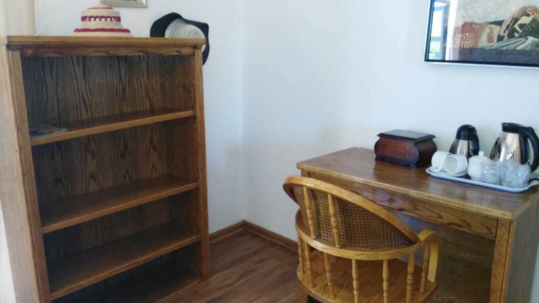 A wooden desk with a wicker chair, a small shelf, and a framed picture on the wall.