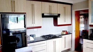 A kitchen with light wooden cabinets, a gas stove, a microwave, and a washing machine. - Lapeng Habo Bantu (Mafeteng)