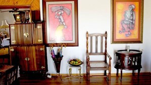 A room with wooden paneling, a wooden chair, a small table with fruit, and two framed artworks on the wall. - Lapeng Habo Bantu (Mafeteng)