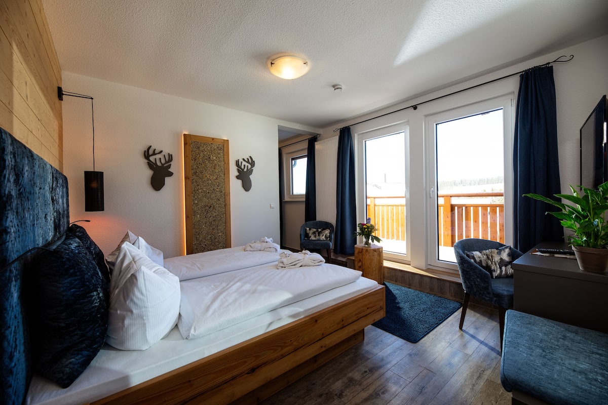 Een moderne slaapkamer met een houten bed, een stoel, een bureau en uitzicht op het groen.