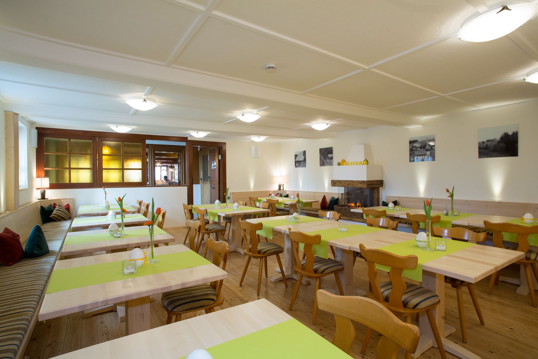 Ein Restaurant mit mehreren Tischen, Stühlen, einem Kamin und Blick durch ein Fenster.