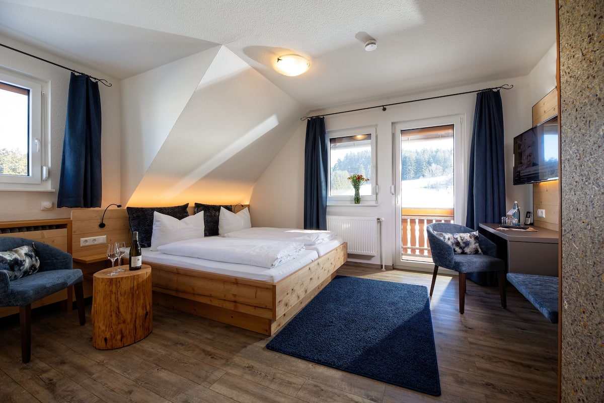 Een slaapkamer met een bed, twee stoelen, een klein tafeltje, een televisie en een raam met gordijnen.