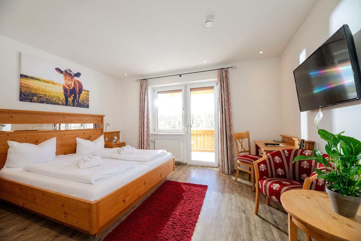 Een slaapkamer met een houten bed, een rode vloerkleed, een bureau, een stoel, een televisie en een plant.