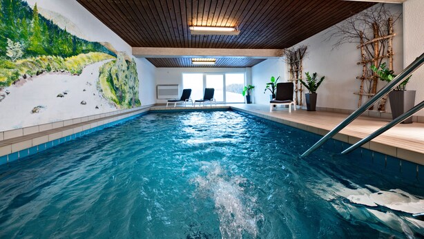 An indoor swimming pool with a wooden ceiling, a mural of a mountainous landscape, and a few lounge chairs.