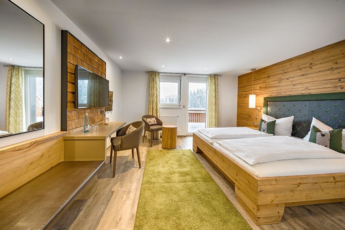 Een moderne hotelkamer met een houten accentmuur, een groot bed, een bureau met stoel en een televisie.
