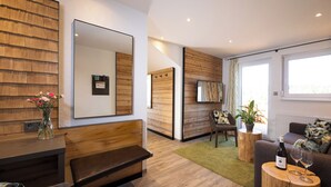 A modern living room with a wooden bench, a sofa, a coffee table, and a large mirror on the wall.