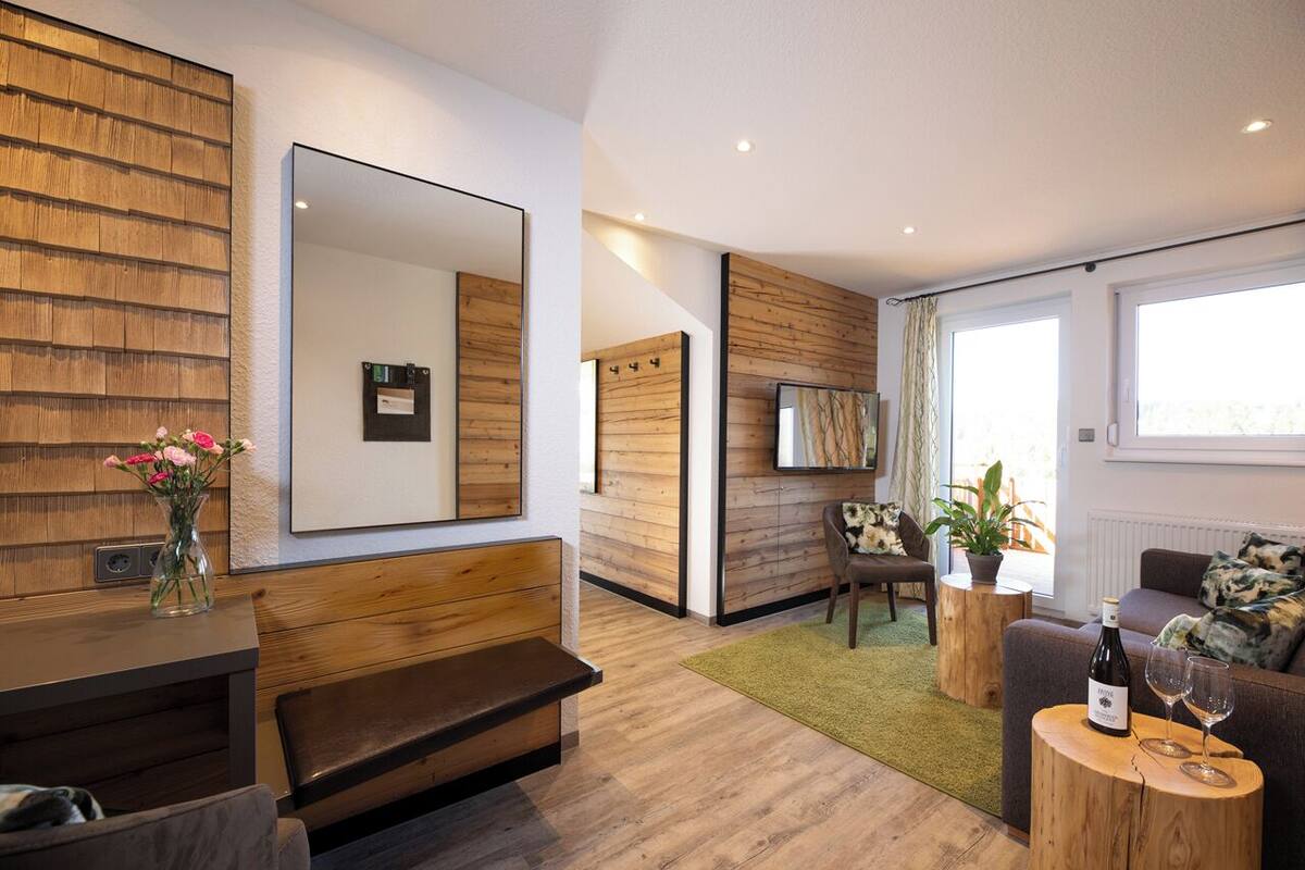 Een moderne woonkamer met een houten bank, een slaapbank, een salontafel en een grote spiegel aan de muur.