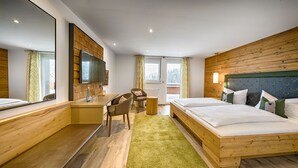 A modern hotel room with a wooden headboard, a large bed, a desk with a chair, and a large mirror.