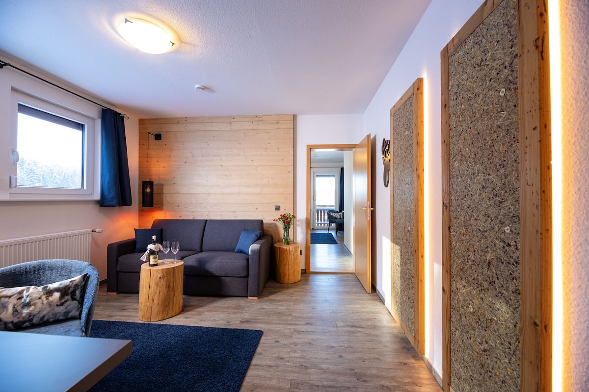 Een moderne woonkamer met een bank, houten details en uitzicht op een andere kamer.