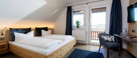 A bedroom with a wooden bed, a desk, a chair, a TV, and a balcony with a plant.