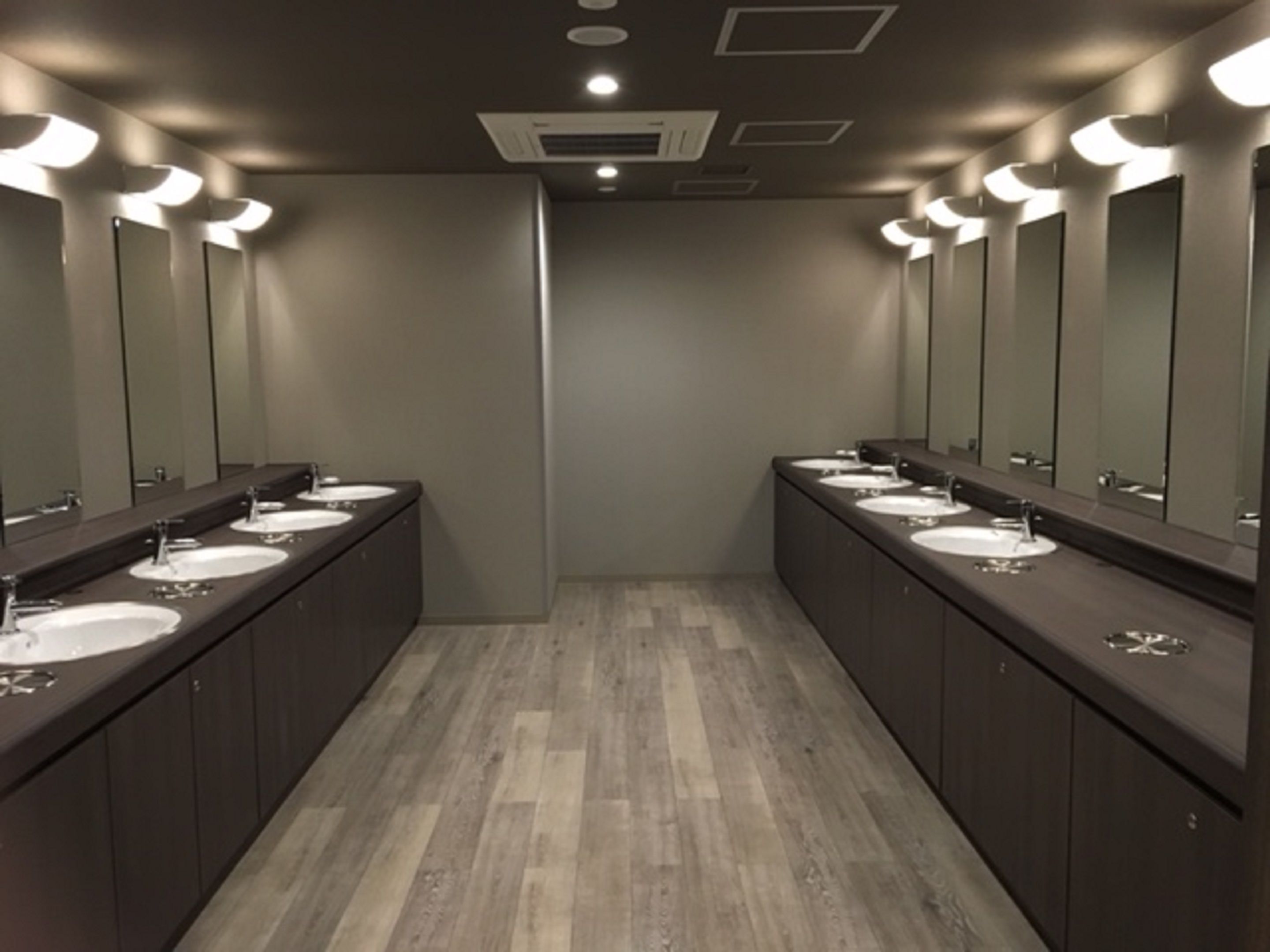 A modern bathroom with multiple sinks and mirrors, wooden flooring, and recessed ceiling lights.