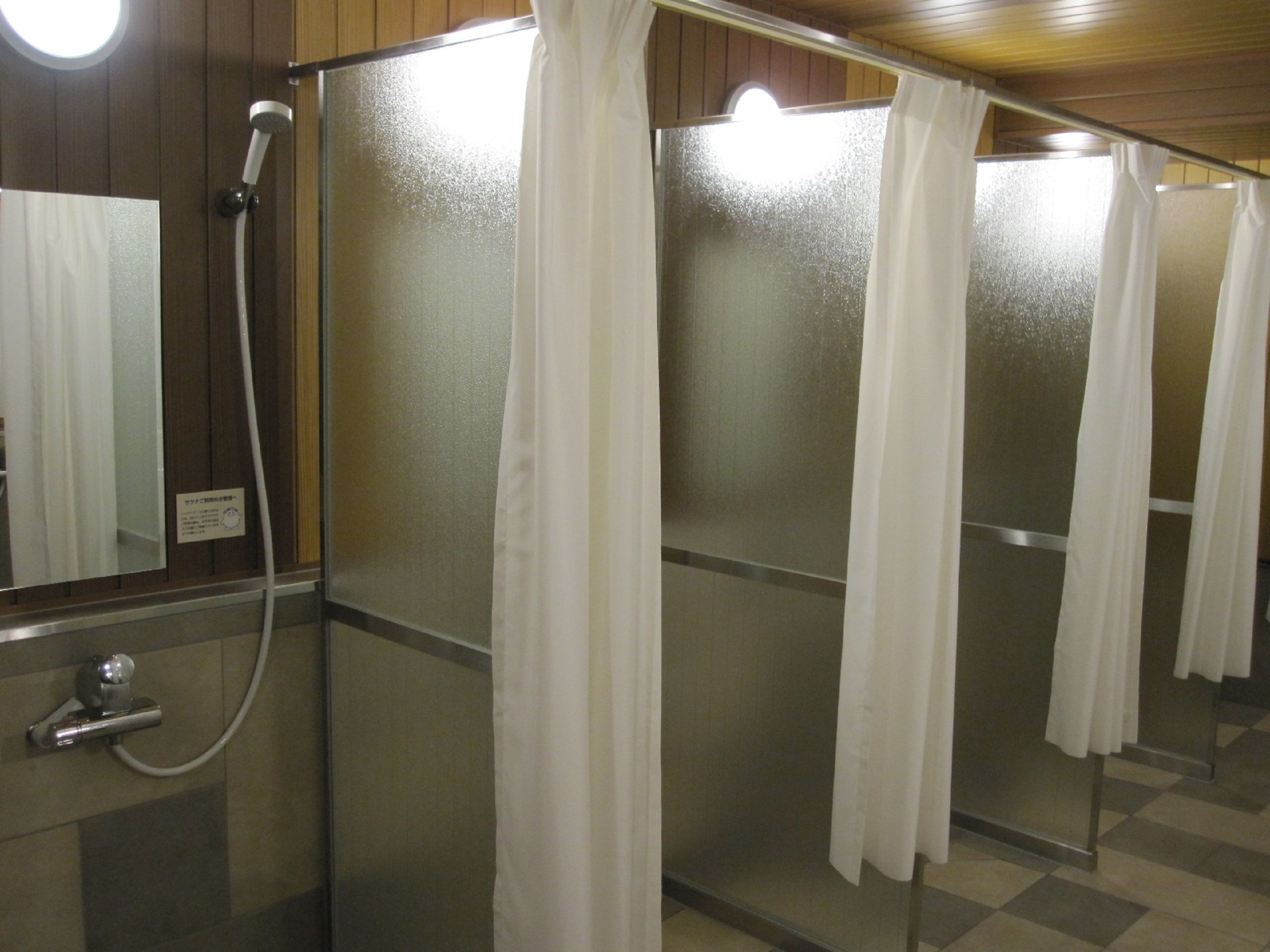 Une rangée de cabines de douche séparées par des cloisons en verre dépoli et dotées de rideaux blancs.