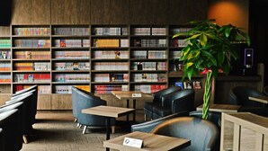 Una biblioteca con estanterías, asientos y una planta.