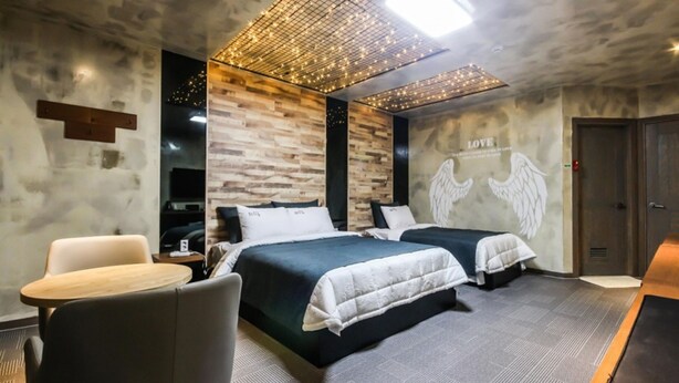 Habitación de hotel con dos camas, un escritorio y una silla. Se observa una pared con diseño de paneles de madera y un techo con una estructura de luces.
