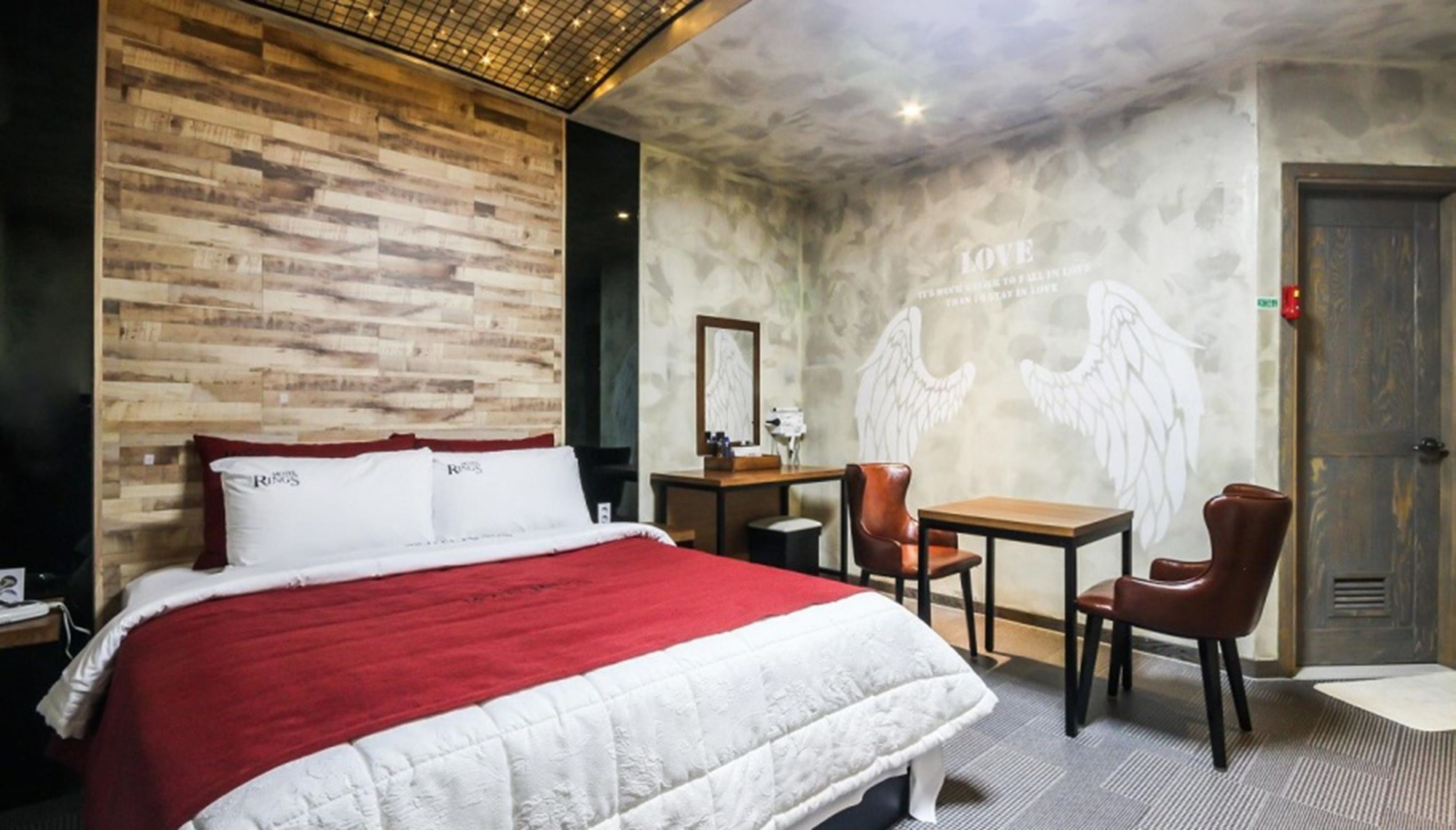 Habitación de hotel con una cama grande, un escritorio, dos sillas, un espejo y una pared con un mural de ángeles.