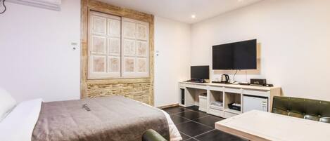A hotel room with a bed, a desk with a computer, a television, and a small table.