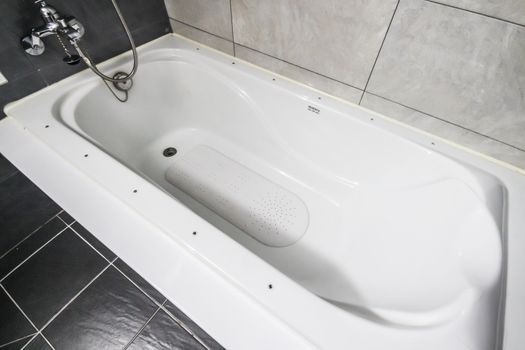 Een wit bad met een handdouche, voor een betegelde muur.