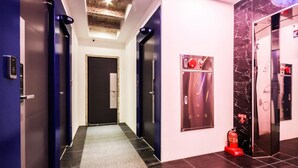 Pasillo de hotel con alfombra negra y gris, un extintor y una pared de mármol.
