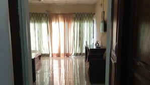 A hallway with a tiled floor, a ceiling fan, and a view into a room with a desk and curtains. - The Weavers Hotel (Abuja)