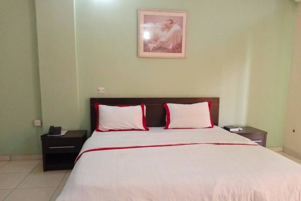 A bedroom with a bed, two nightstands, a framed picture on the wall, and a tiled floor.