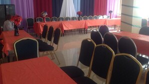 A conference room with rows of tables and chairs, draped with red and blue curtains. - The Weavers Hotel (Abuja)