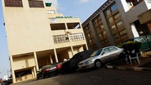 A multi-story building with a parking area in front. - The Weavers Hotel (Abuja)