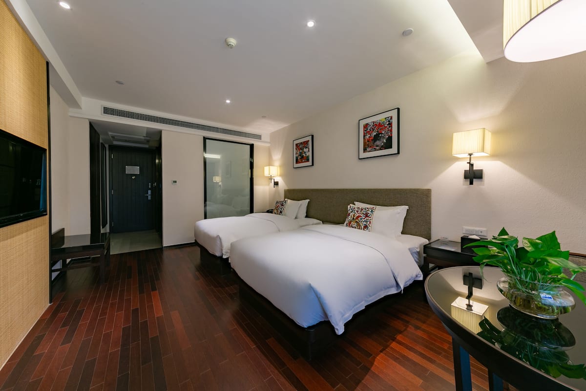 A hotel room with two beds, a bedside table, a lamp, a plant, and a TV.