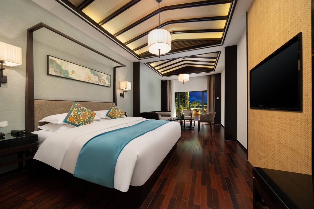 A modern hotel room with a large bed, a desk, a chair, a TV, and a view of the outdoors.