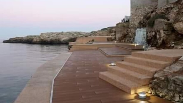 Un paseo marítimo con escalones que conducen a un acantilado rocoso, con vista al mar.