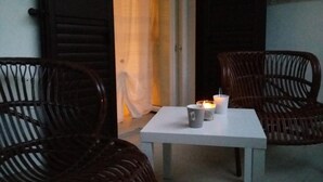 Un pequeño espacio al aire libre con dos sillas de mimbre y una mesa blanca, con una vela y una taza.