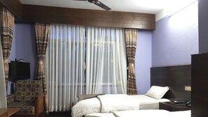 Een hotelkamer met een bed, een bureau, een stoel, een televisie en een raam met gordijnen.