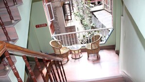 Een trap met houten spijlen die leidt naar een balkon met rieten meubilair en uitzicht op de straat eronder.