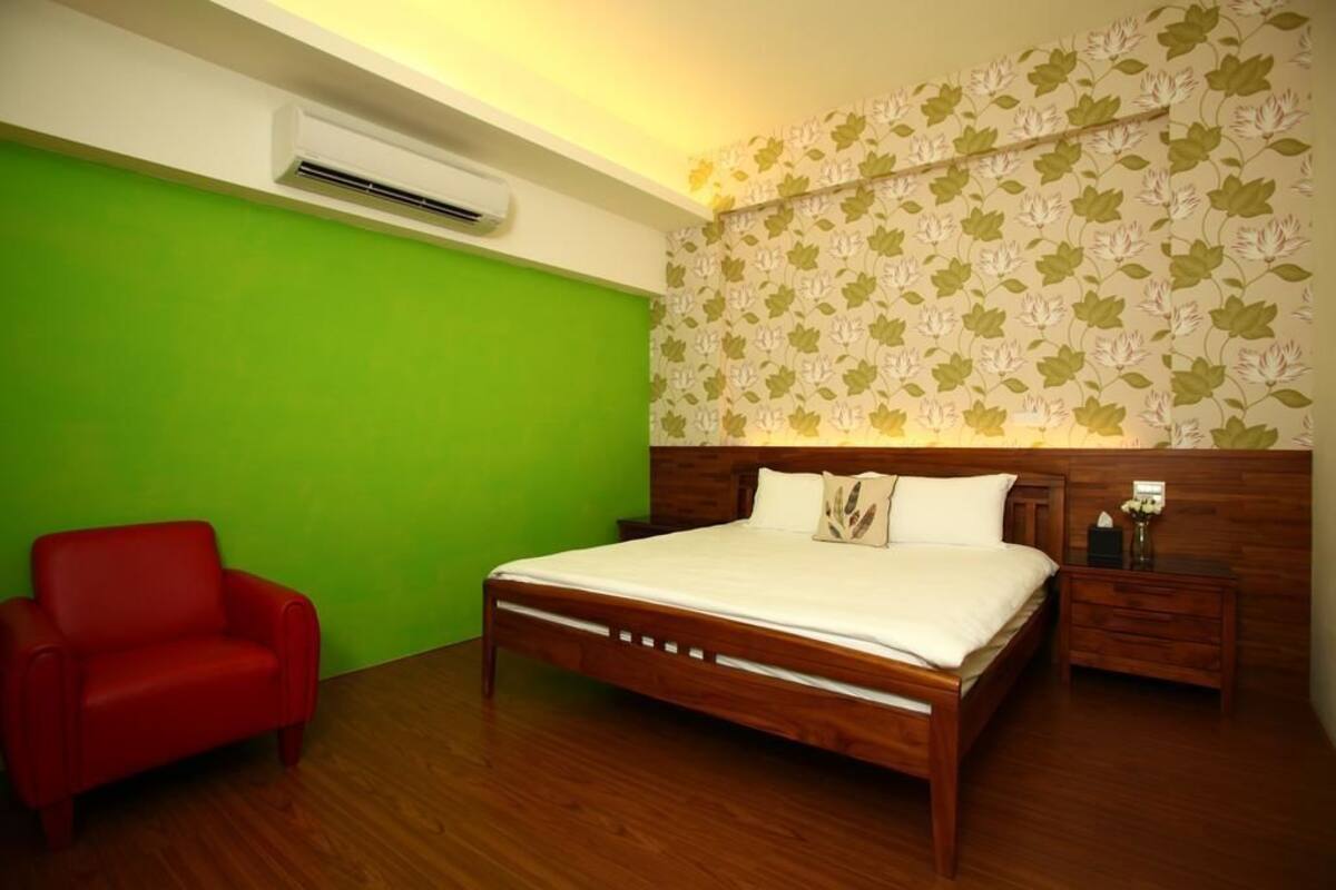 A bedroom with a wooden bed, a red chair, a nightstand, and a wall with floral wallpaper.