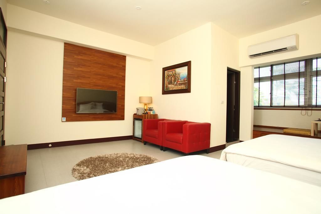 Una habitación de hotel con una cama grande, un sofá rojo, un televisor montado en la pared y un cuadro.