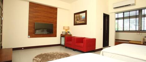 Una habitación de hotel con una cama grande, un sofá rojo, un televisor montado en la pared y un cuadro.