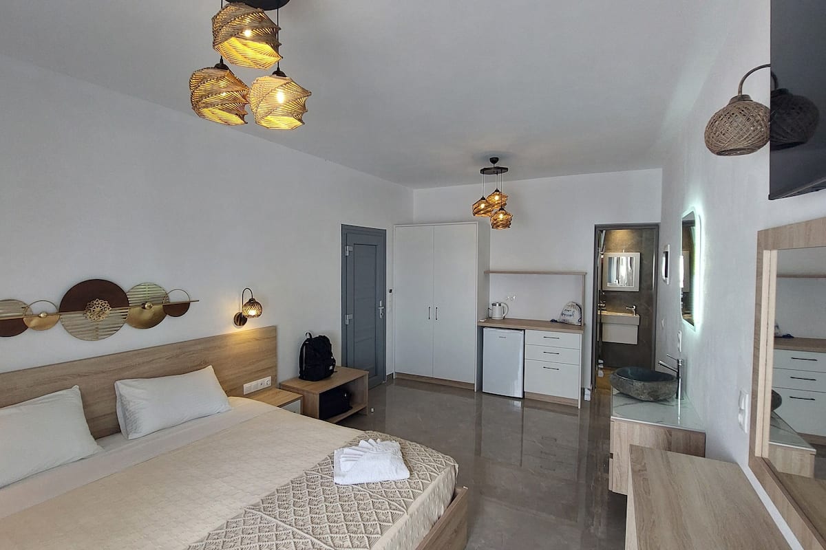 A modern hotel room with a large bed, bedside tables, a wardrobe, a bathroom with a mirror, and hanging lights.